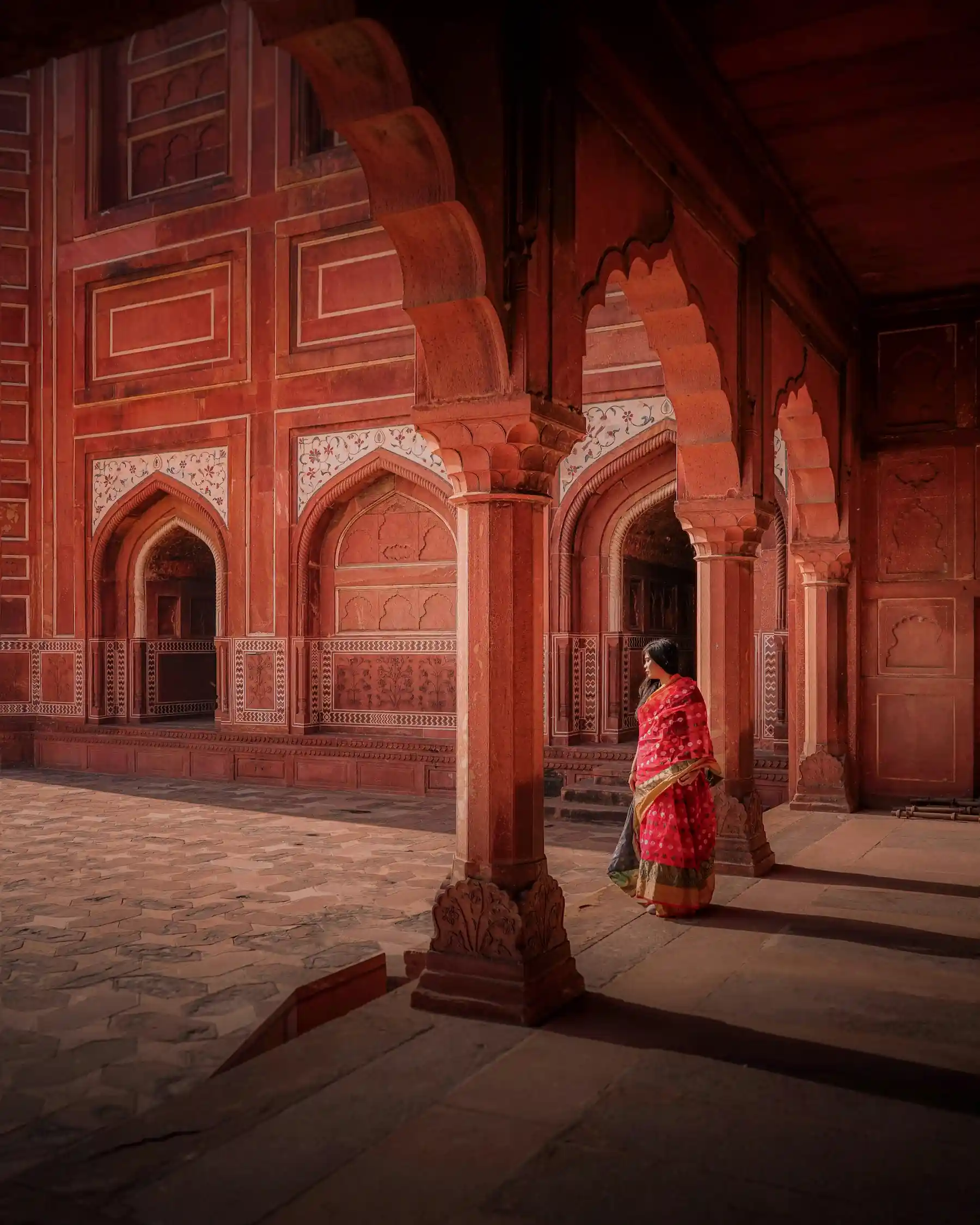 Donna con sari rosso nel cortile del forte rosso agra circondata dagli archi in arenaria rossa